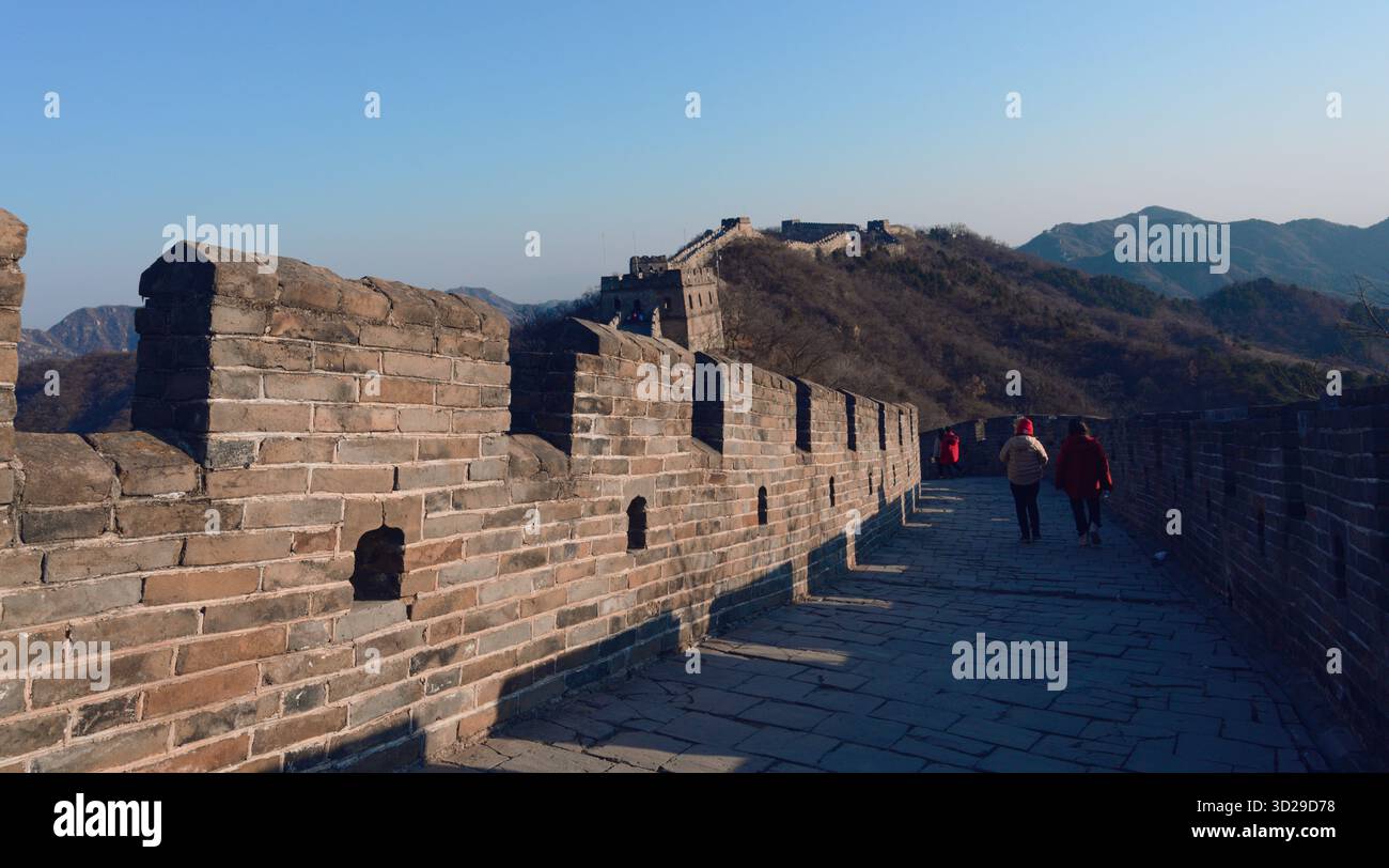 Der alte Steinweg der Chinesischen Mauer, der sich über die zerklüfteten Hügel schlängelt, im Winterlicht unter hellem Himmel getaucht Stockfoto