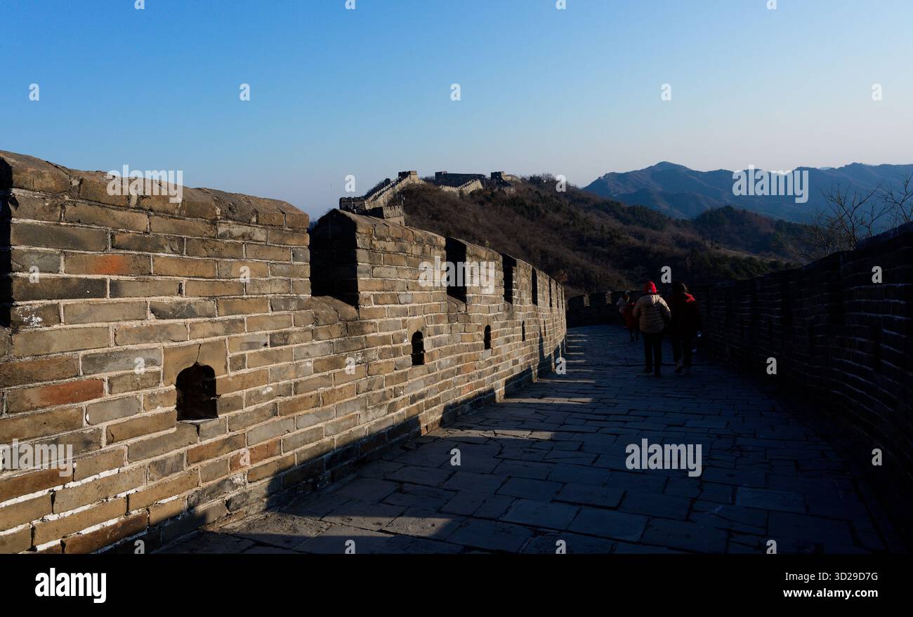 Die Chinesische Mauer, die sich über die zerklüfteten Hügel schlängelt, in hartes Winterlicht unter einem hellen Himmel getaucht Stockfoto