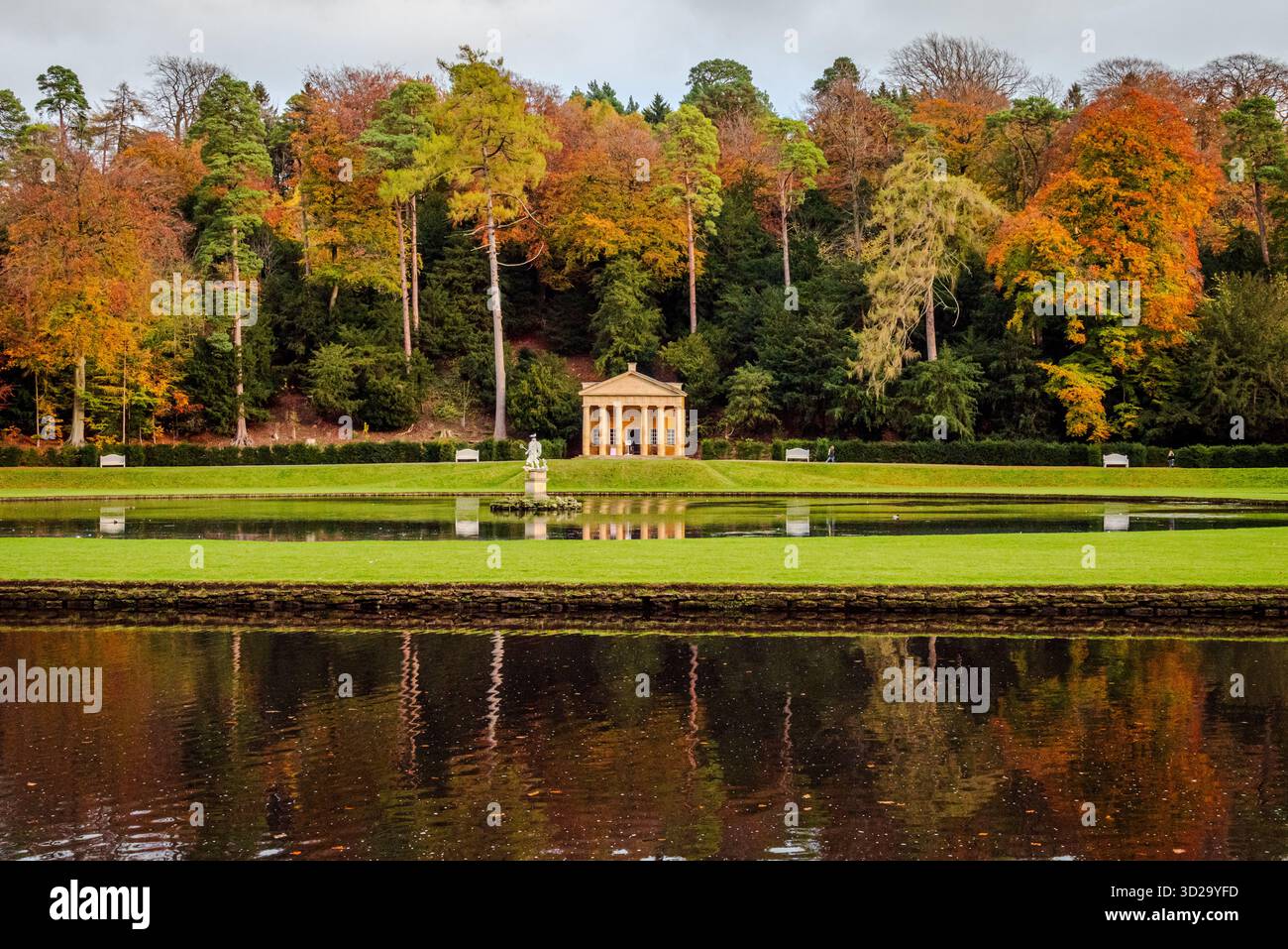 Ein kurzer Blick auf den Studley Royal Water Garden in North Yorkshire, mit Bäumen und Wasser, die warme Herbstfarben unter weichem, saisonalem Licht reflektieren Stockfoto