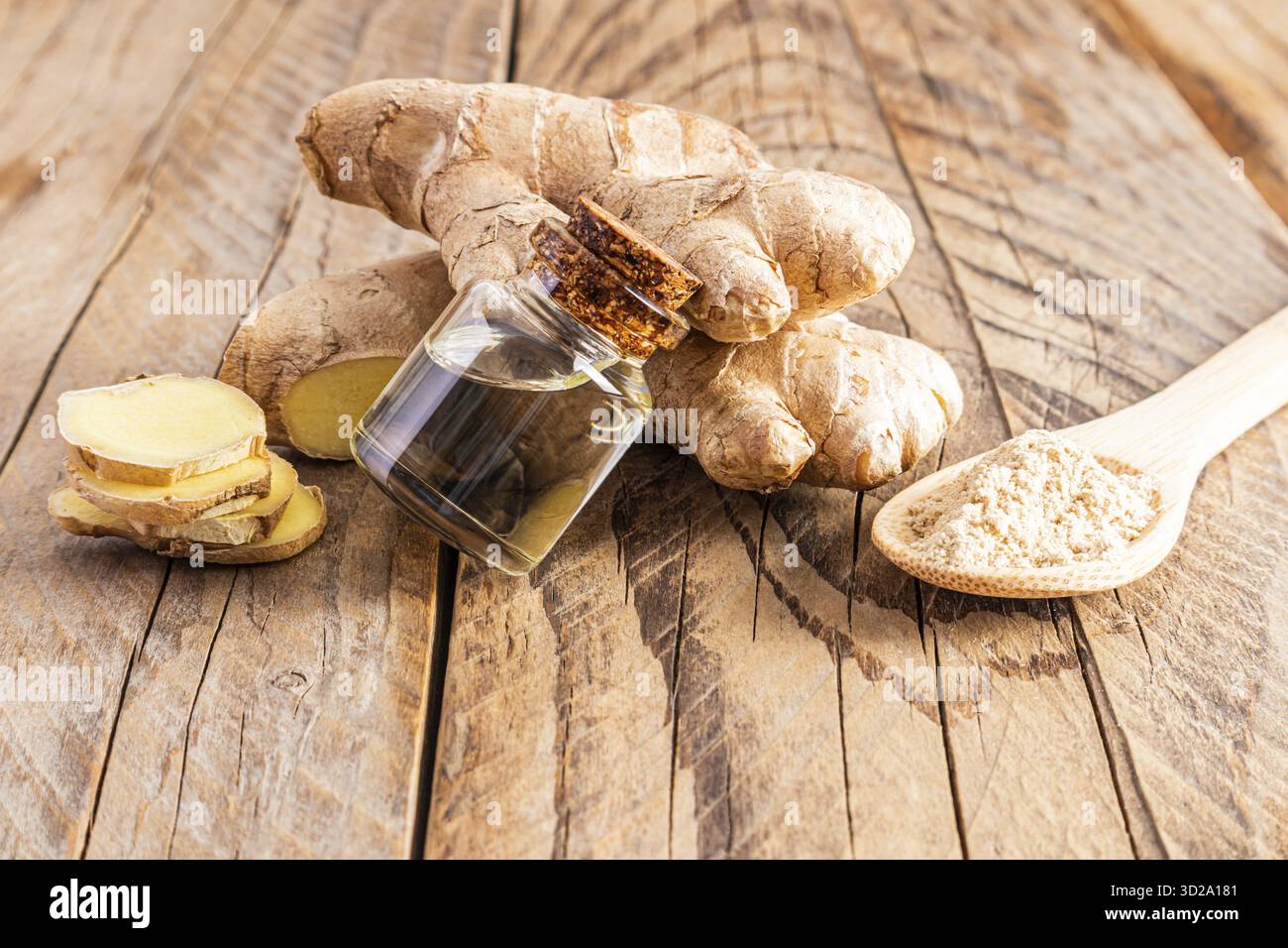 Eine Flasche ätherisches Ingwerwurzelöl aus biologischem Anbau liegt auf einer großen Pflanzenwurzel und einem Holztisch. Natürliches Selbstpflegekonzept, Aromatherapie, Spa Stockfoto