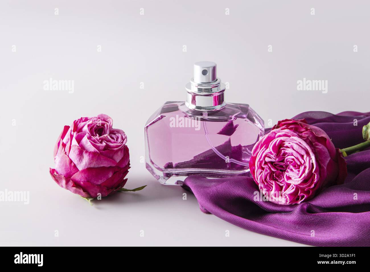 Elegantes Glas mit Damenparfüm, zarten Rosenknospen und lila Chiffon-Schal für Damen. Darstellung des Duftes Stockfoto