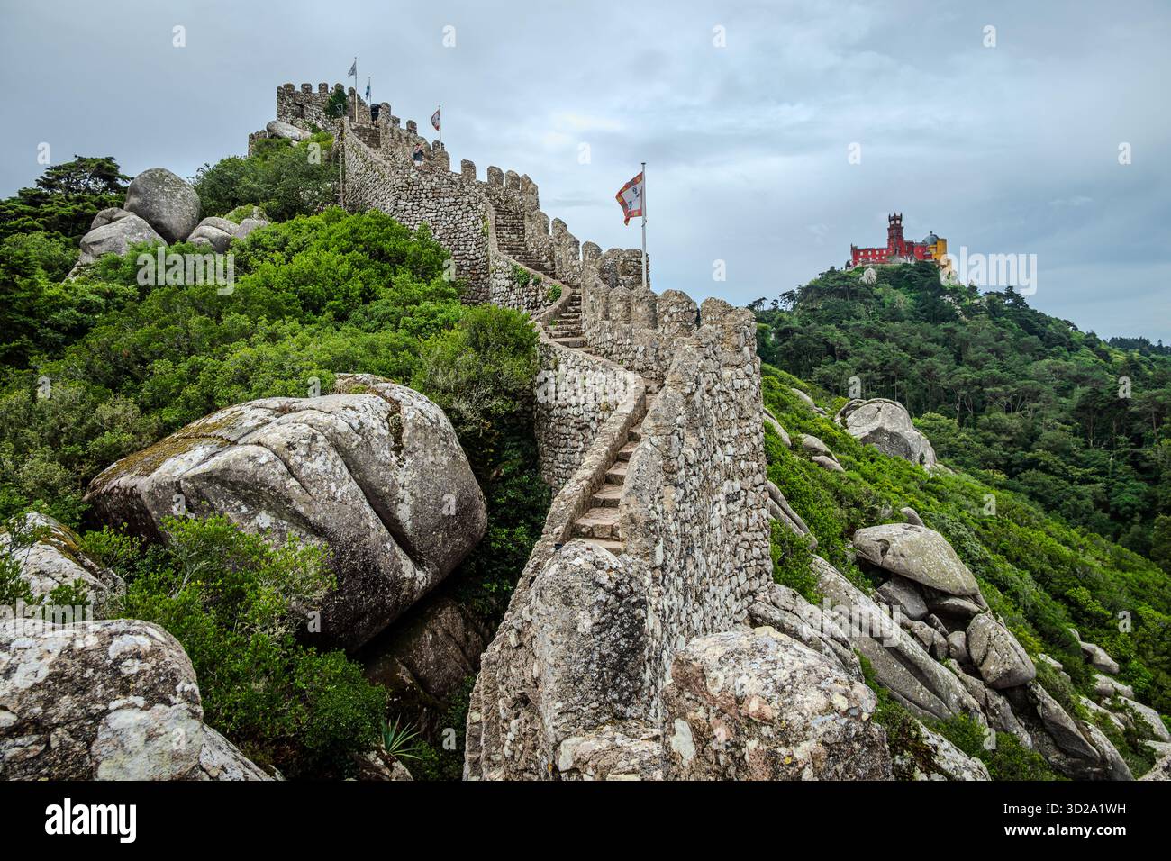 Alte Steinmauer der maurischen Burg auf einem felsigen Hügel mit dem Palast von Pena sichtbar in der Ferne, Sintra, Portugal Stockfoto