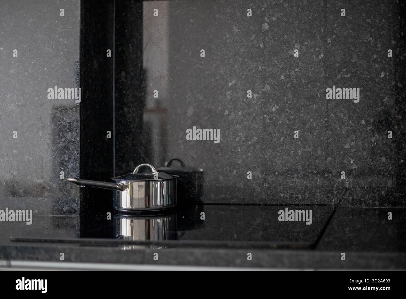 Edelstahl-Topf mit Deckel sitzt auf einem modernen schwarzen Küchenherd. Die saubere Arbeitsplatte und der Fokus auf Kochgeschirr betonen Einfachheit und Funktionalität Stockfoto