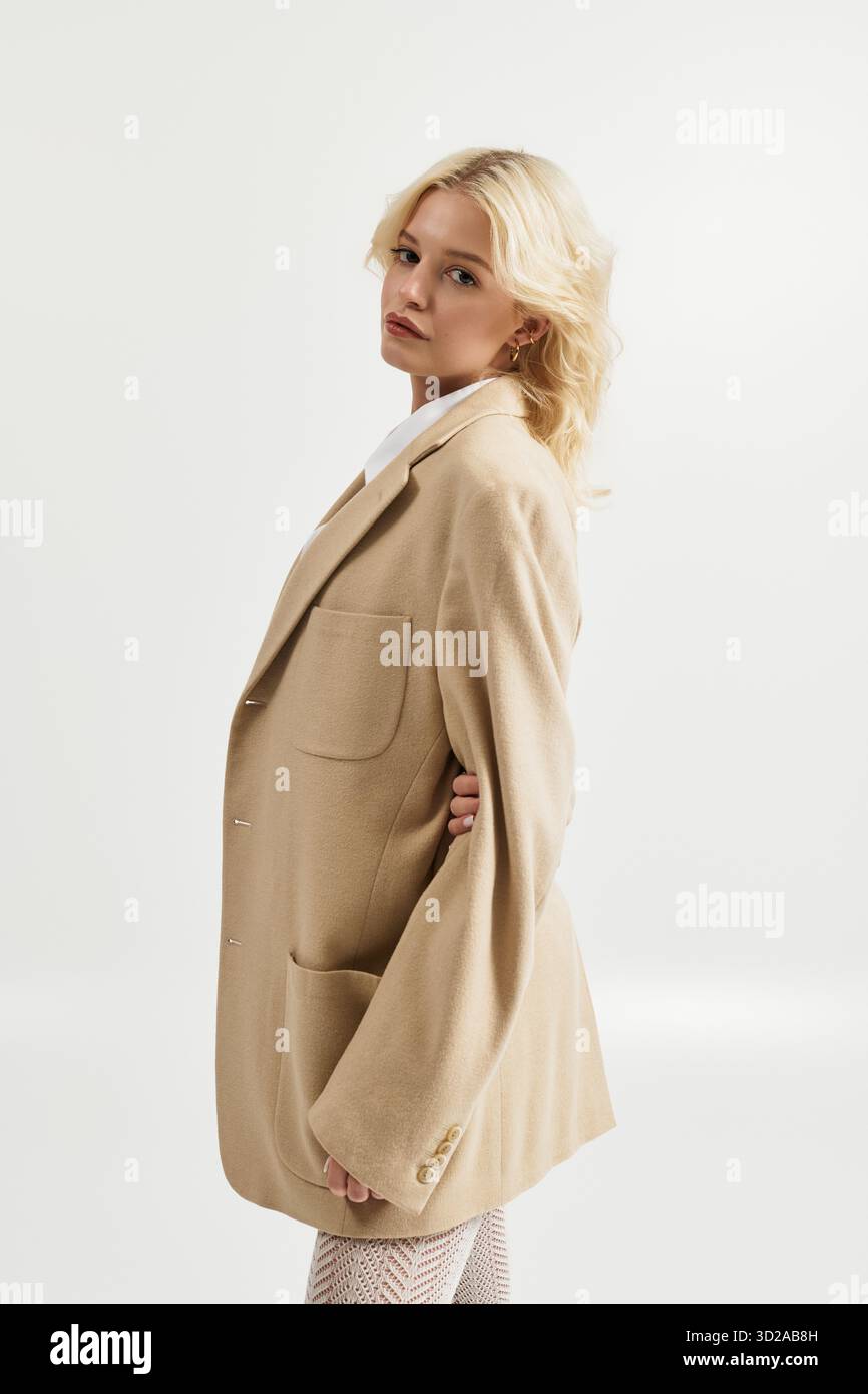 Eine schöne junge blonde Frau zeigt ein trendiges Winteroutfit in einem hellen, weißen Studio. Stockfoto