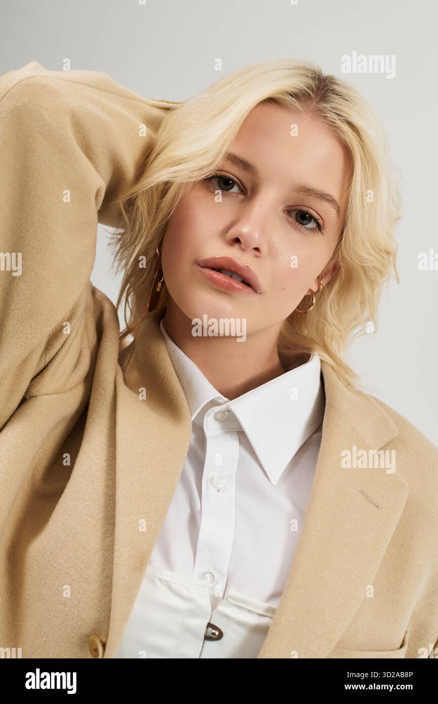 Die blonde Frau in schickem Outfit posiert anmutig in einem modernen weißen Studio-Setting. Stockfoto