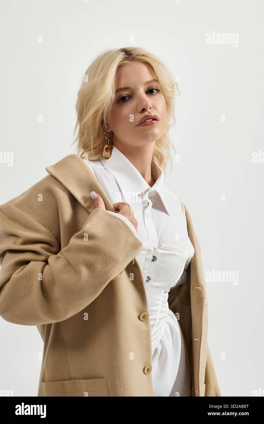 Eine schöne blonde Frau präsentiert ein trendiges Winteroutfit in einem hellen weißen Studio. Stockfoto