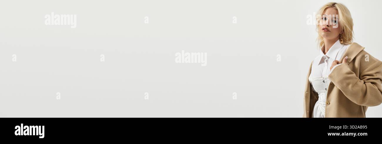 Eine schöne blonde Frau zeigt ein trendiges Winteroutfit, während sie in einem hellen weißen Studio posiert, Banner Stockfoto