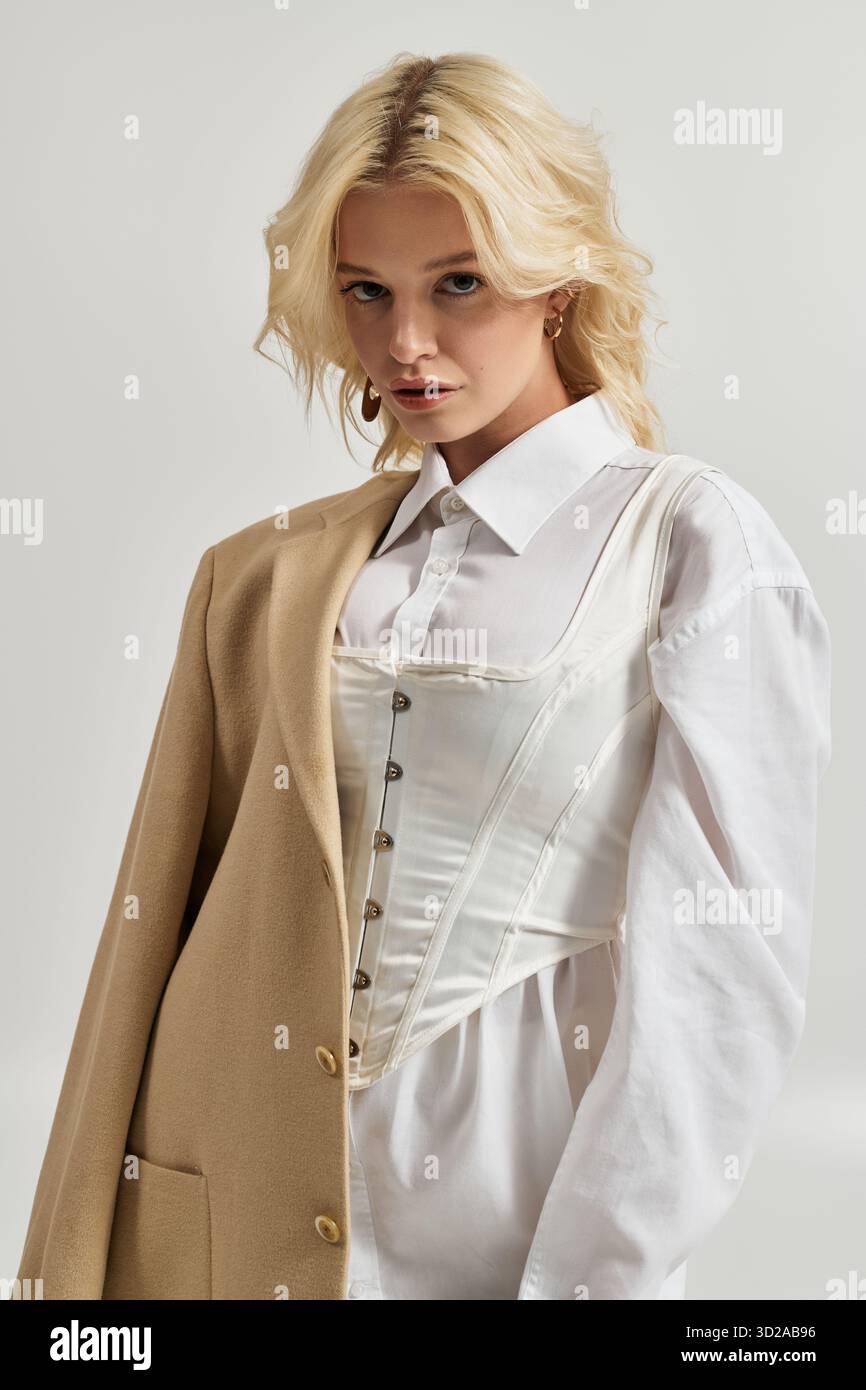 Eine schöne junge blonde Frau posiert selbstbewusst in einem schicken Winteroutfit in einem weißen Studio. Stockfoto