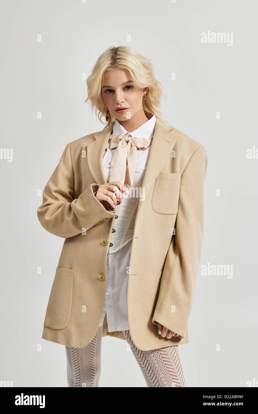 Eine schöne junge blonde Frau modelliert ein trendiges Winteroutfit in einem minimalistischen weißen Studio. Stockfoto