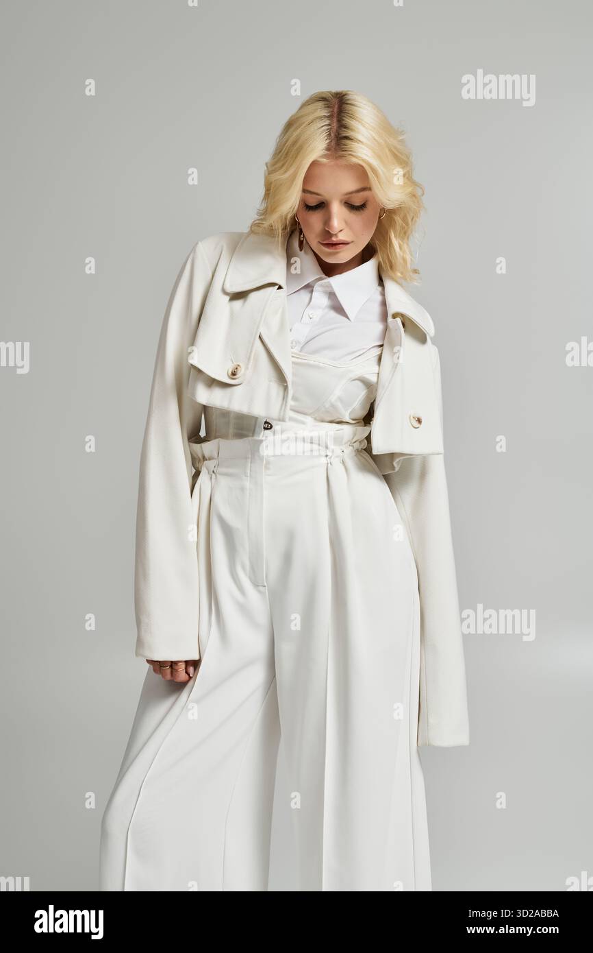 Stilvolle junge Frau posiert in trendigem weißem Outfit in hellem Studio, das Mode umgibt. Stockfoto