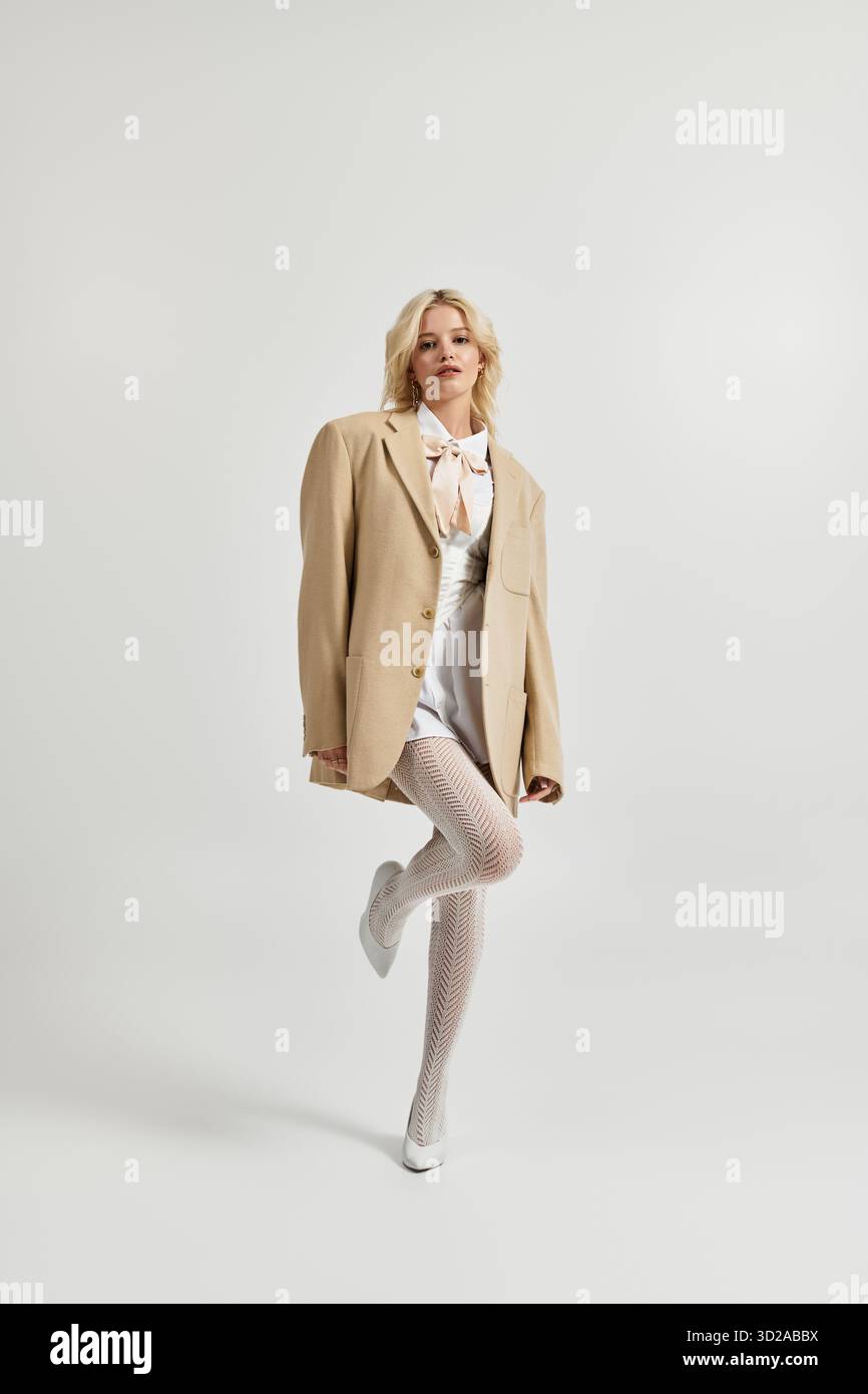 Eine schöne junge blonde Frau posiert selbstbewusst in einem weißen Studio und trägt trendige Winterkleidung. Stockfoto