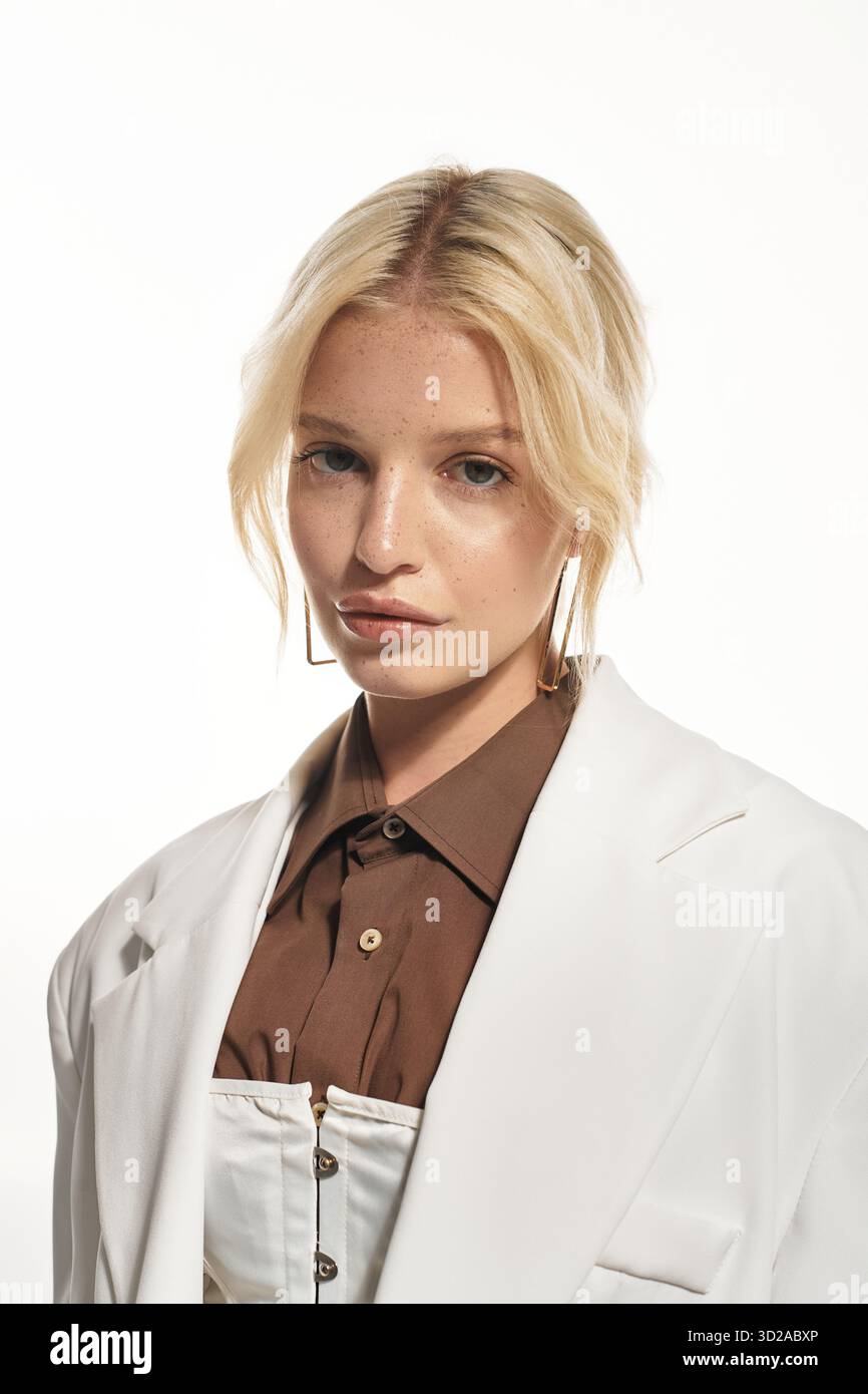 Eine schöne blonde Frau posiert selbstbewusst in einem stilvollen Outfit in einem hellen weißen Studio. Stockfoto