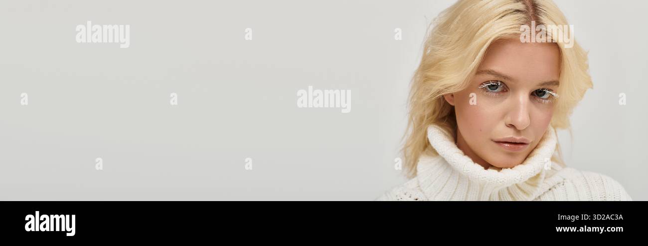 Eine junge blonde Frau mit einzigartigen weißen Wimpern posiert in einem gemütlichen Strickpullover, Banner Stockfoto