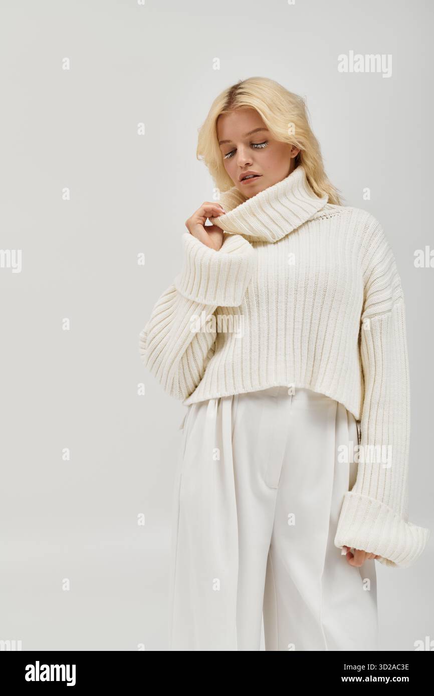 Eine junge blonde Frau mit weißen Wimpern posiert anmutig in einem gemütlichen Pullover und strahlt Wärme aus. Stockfoto