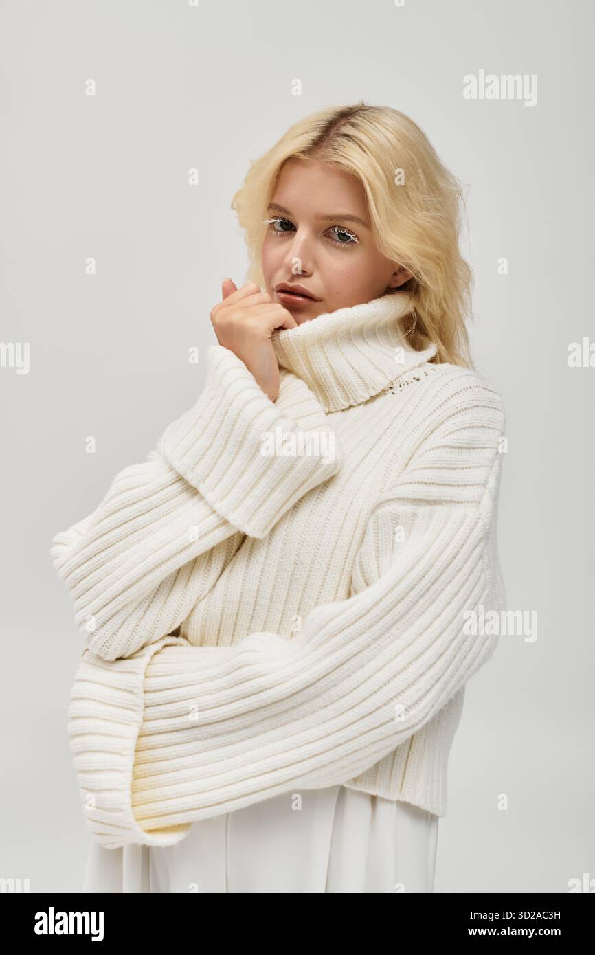 Eine junge Frau mit weißen Wimpern zeigt Stil in einem gemütlichen Strickpullover vor einem weichen Hintergrund. Stockfoto