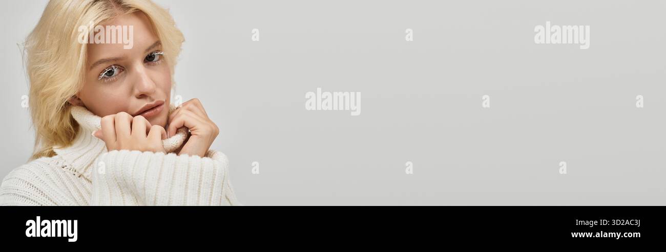 Eine schöne junge blonde Frau posiert warm in einem kuscheligen Strickpullover, strahlt Schönheit aus, Banner Stockfoto