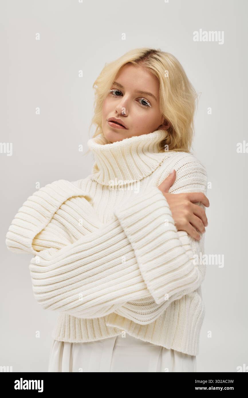 Eine blonde Frau mit auffälligen weißen Wimpern entspannt sich in einem weichen, gemütlichen Pullover, der Schönheit versprüht. Stockfoto