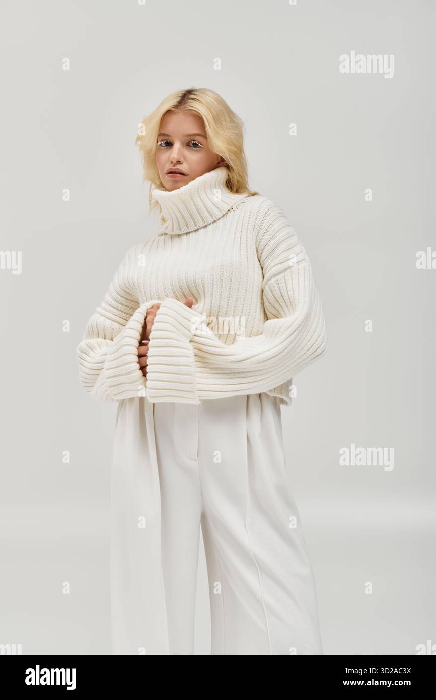 Eine junge blonde Frau posiert anmutig in einem kuscheligen Strickpullover und fängt den Charme des Winters ein. Stockfoto
