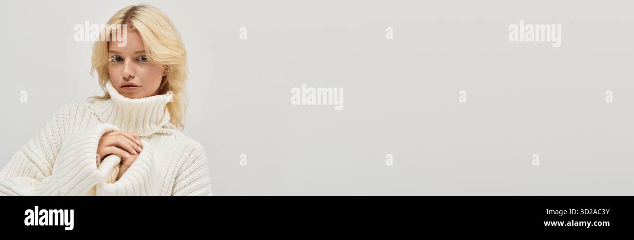 Blonde Frau mit weißen Wimpern steht anmutig in einem gemütlichen Strickpullover, Banner Stockfoto