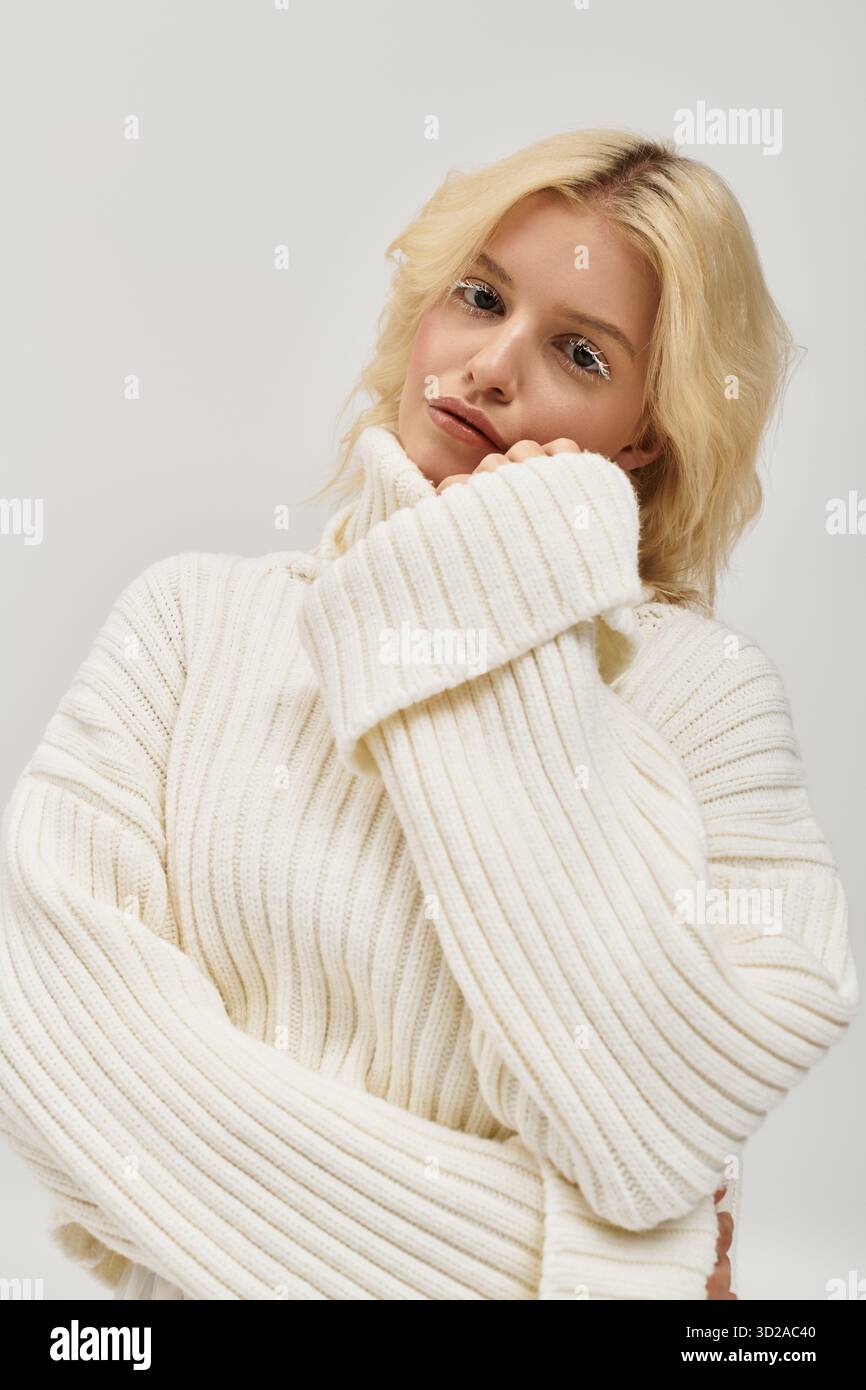 Eine junge blonde Frau mit weißen Wimpern lächelt sanft, während sie einen warmen Strickpullover trägt. Stockfoto