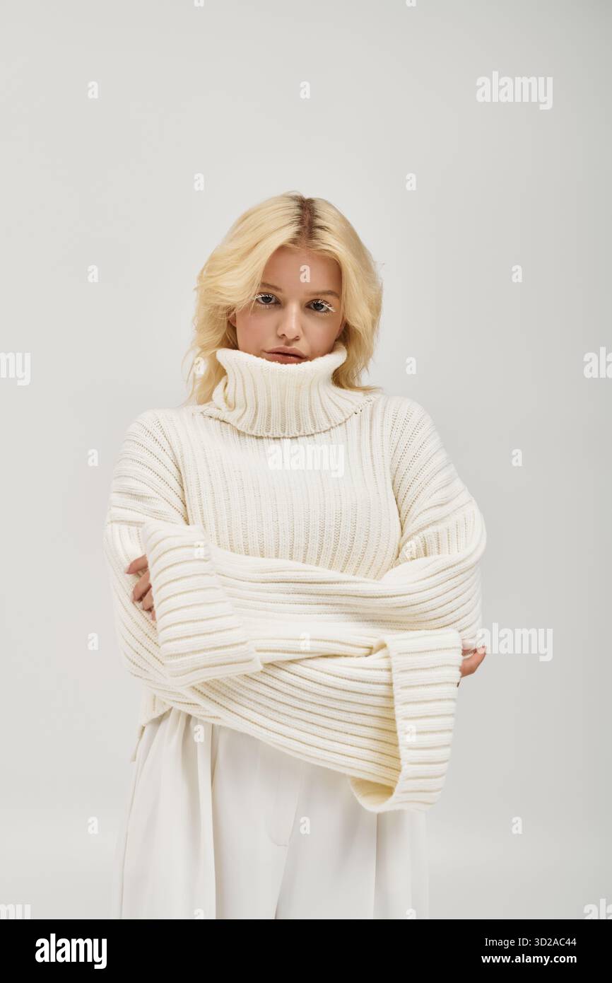 Eine junge blonde Frau mit weißen Wimpern entspannt sich in einem kuscheligen Strickpullover und strahlt Winterzauber aus. Stockfoto