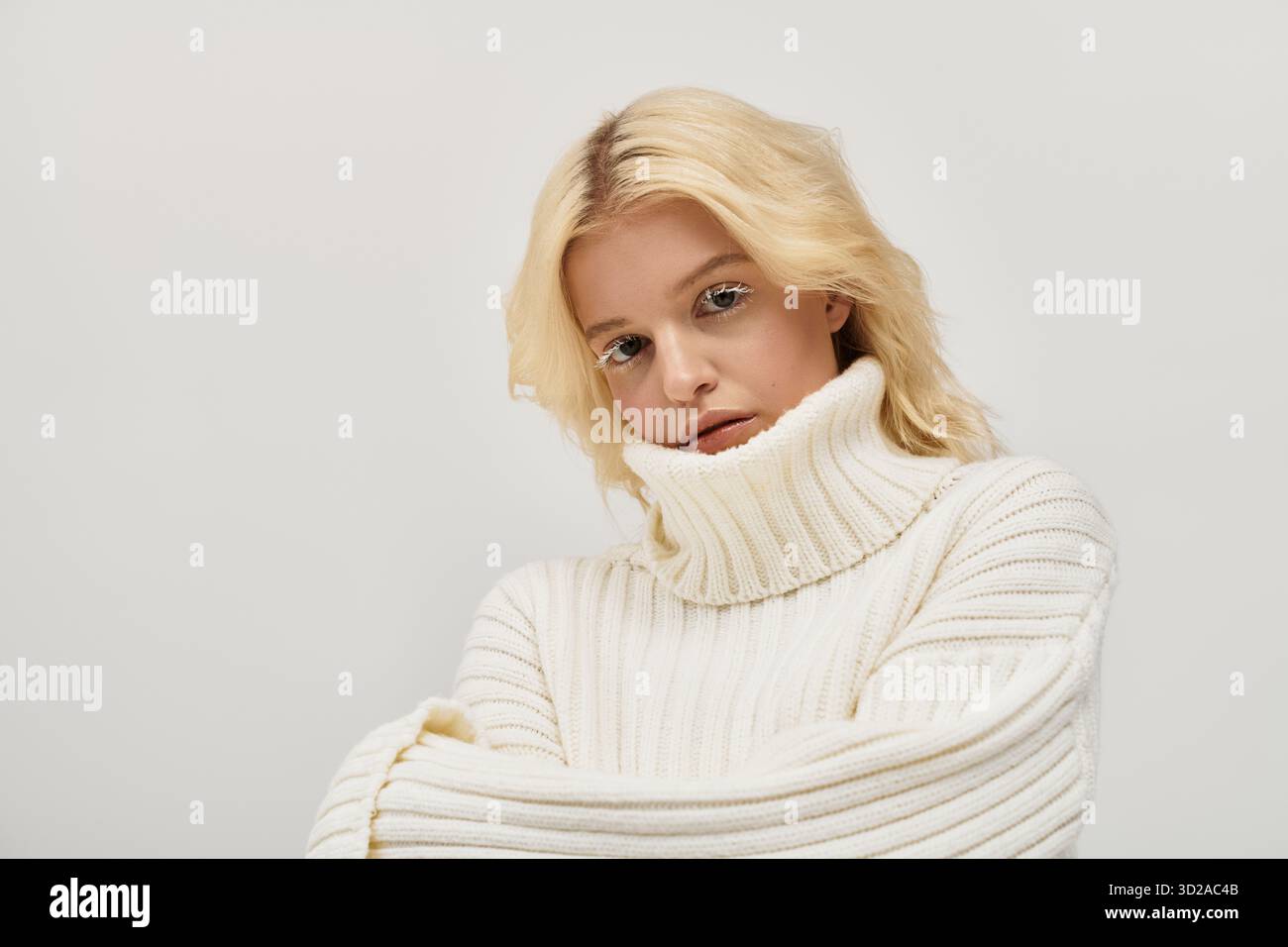 Junge Frau mit schönen blonden Haaren und weißen Wimpern posiert warm in einem Strickpullover. Stockfoto