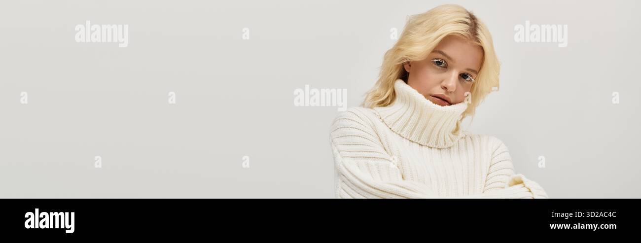Eine junge blonde Frau posiert in einem kuscheligen Strickpullover und zeigt ihre einzigartige Schönheit und ihren Stil, Banner Stockfoto
