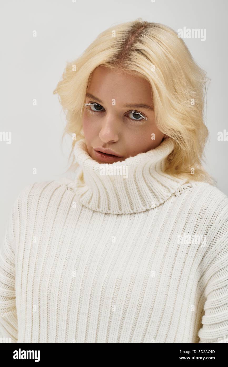 Eine junge blonde Frau posiert selbstbewusst und zeigt ihre weißen Wimpern in einem stylischen Pullover. Stockfoto