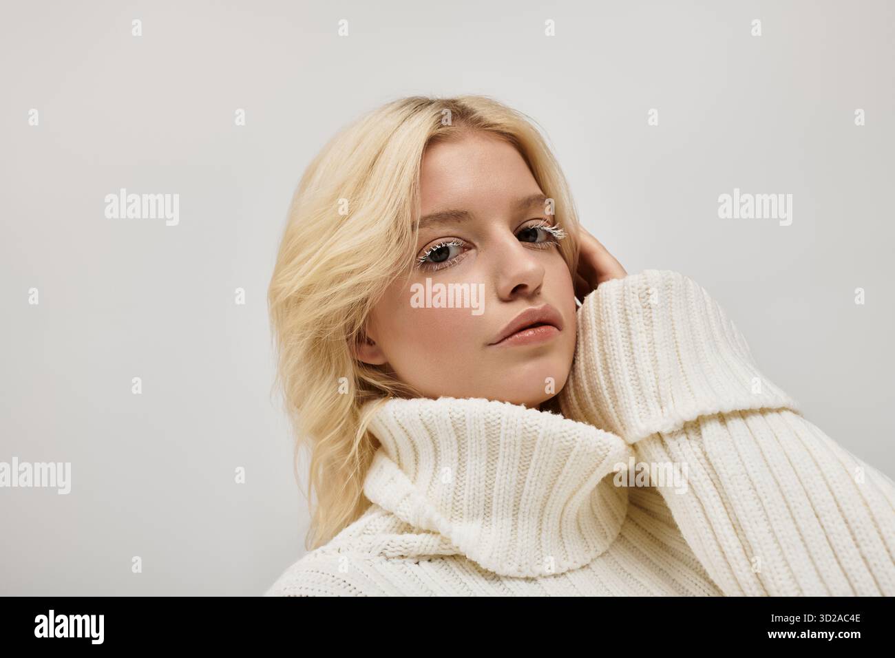Eine schöne junge blonde Frau mit weißen Wimpern posiert in einem gemütlichen Strickpullover in einem Studio. Stockfoto