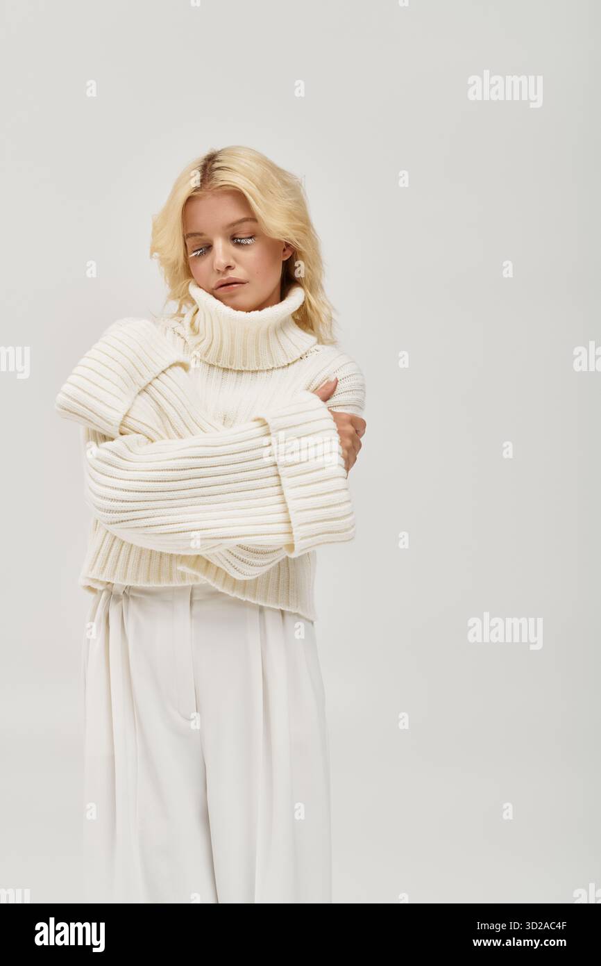 Eine schöne junge blonde Frau posiert selbstbewusst in einem gemütlichen Studio und trägt einen Strickpullover. Stockfoto