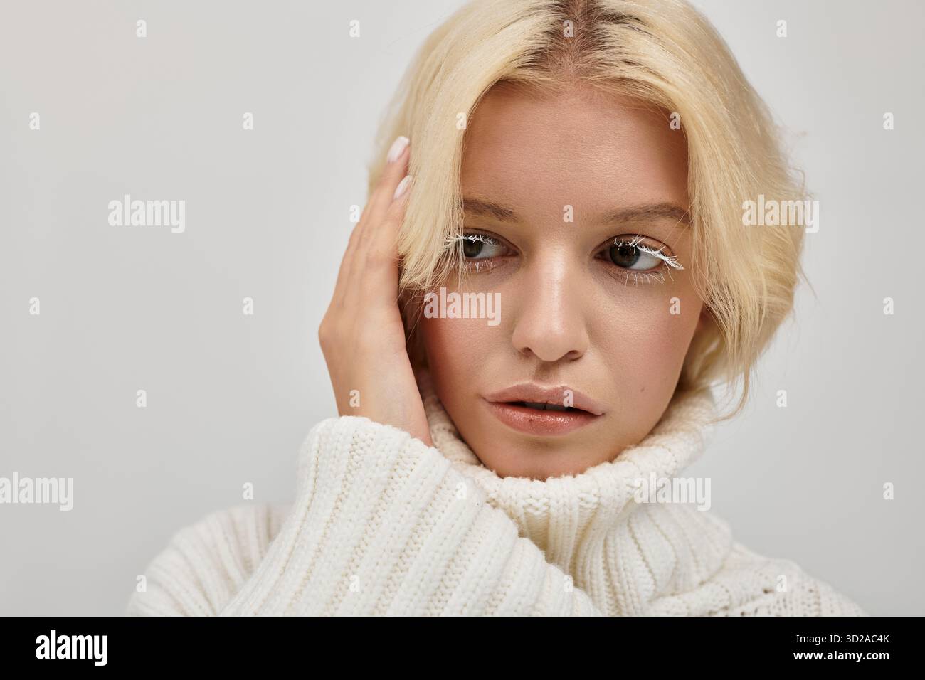 Eine junge blonde Frau mit weißen Wimpern posiert in einem gemütlichen Studio in einem Strickpullover. Stockfoto