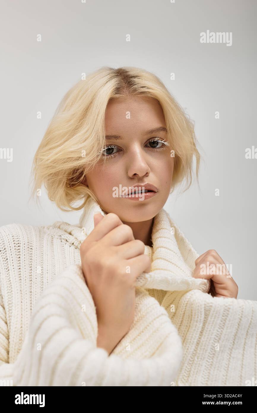 Eine schöne junge Frau mit weißen Wimpern posiert in einem gemütlichen Strickpullover. Stockfoto