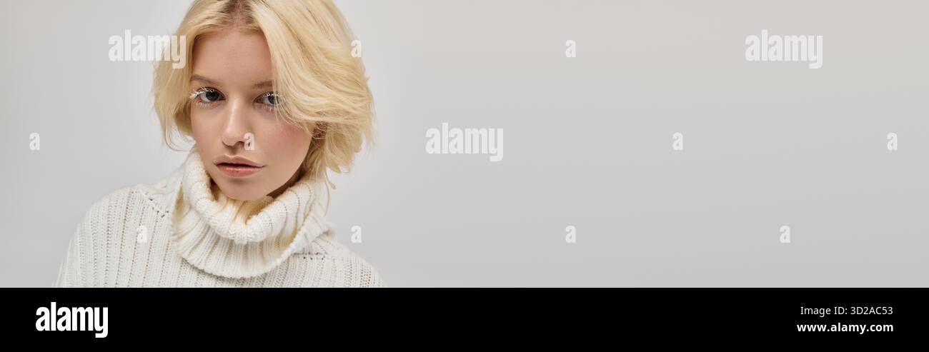 Eine junge blonde Frau mit weißen Wimpern posiert in einem gemütlichen Strickpullover, Banner Stockfoto