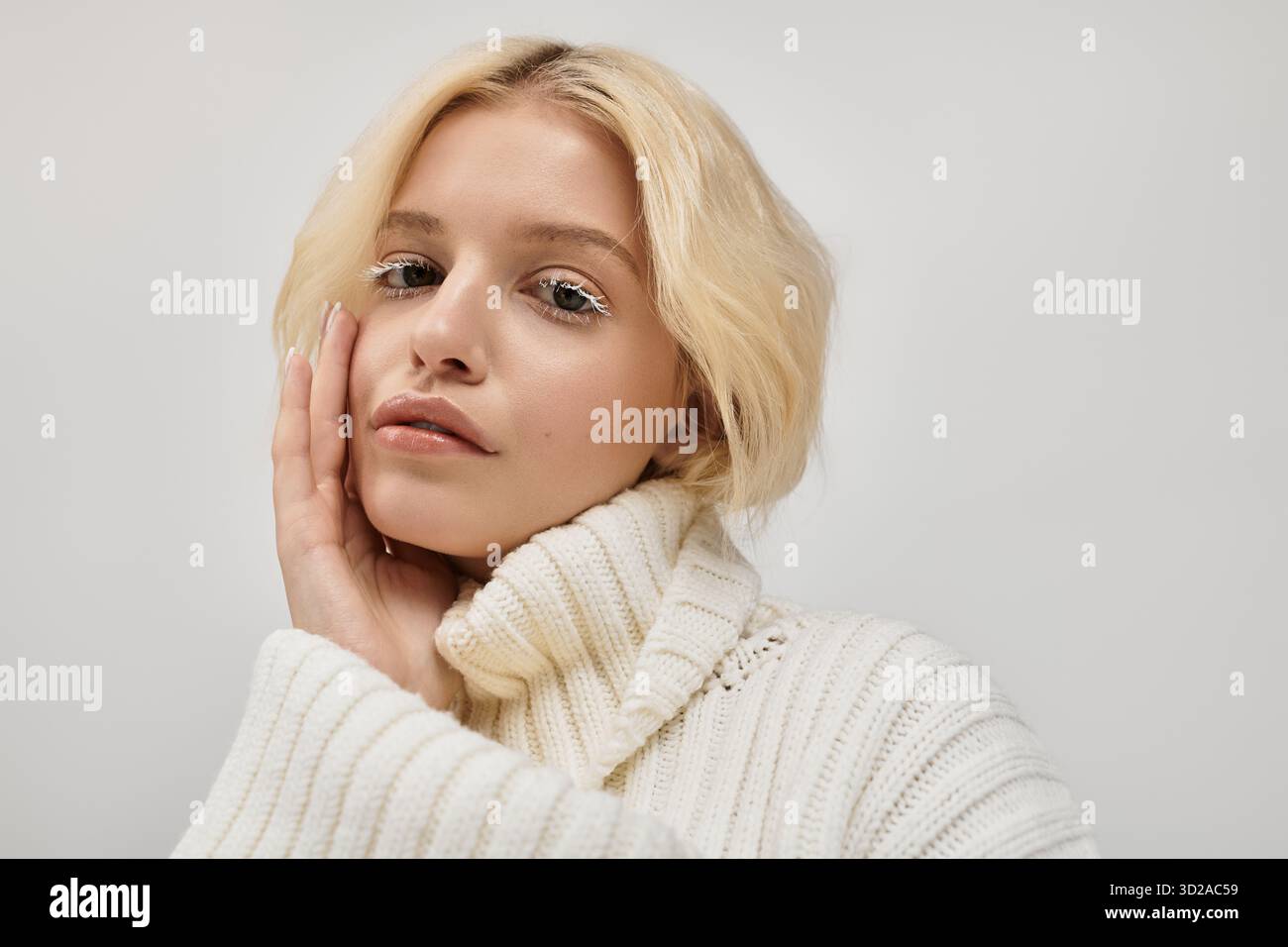 Junge blonde Frau mit weißen Wimpern posiert sanft in einem gemütlichen Studio und zeigt ihre Schönheit. Stockfoto