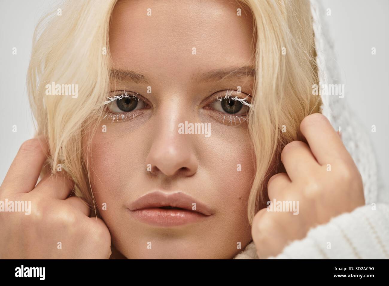 Eine junge blonde Frau mit weißen Wimpern posiert in einem gemütlichen Pullover und strahlt Schönheit aus. Stockfoto