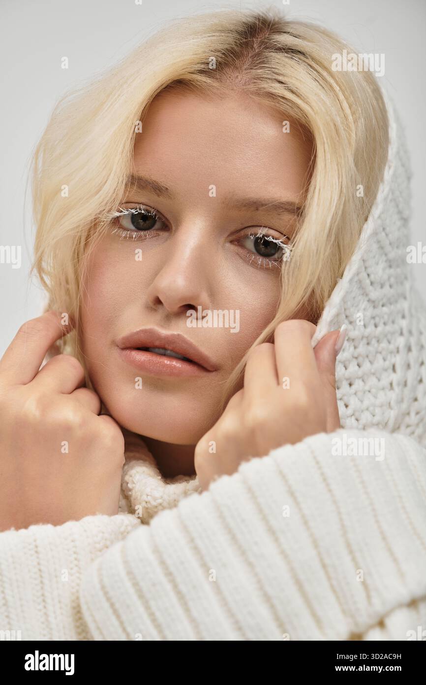 Eine schöne blonde Frau mit weißen Wimpern posiert in einem gemütlichen Pullover und strahlt Wärme aus. Stockfoto