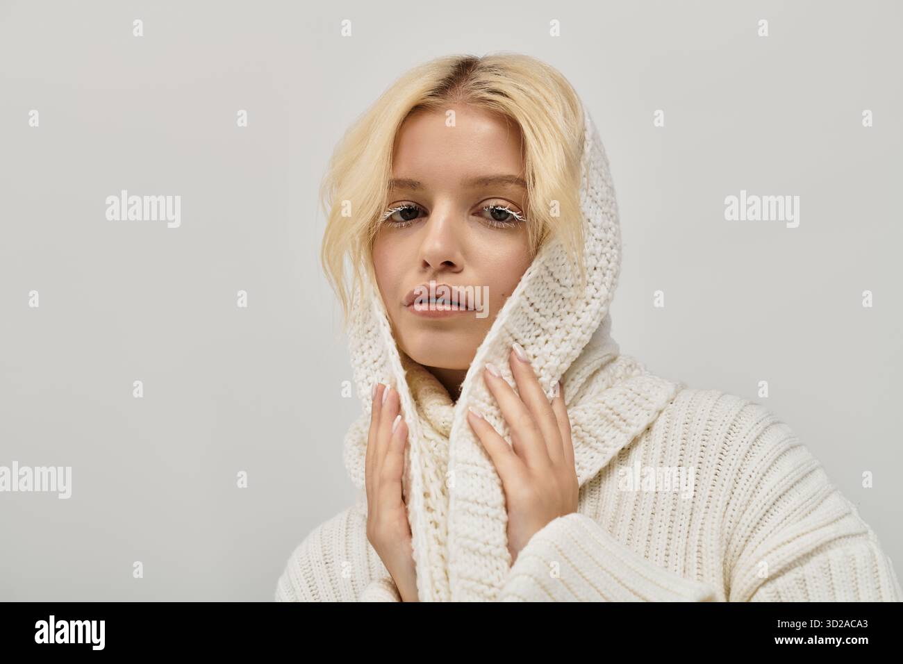 Die blonde Frau mit weißen Wimpern posiert anmutig in einem gemütlichen Strickpullover und zeigt Eleganz. Stockfoto