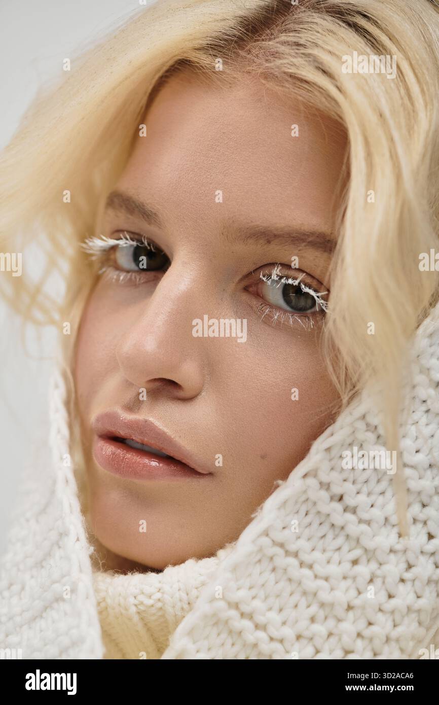 Eine hübsche blonde Frau posiert in einem weichen Pullover und hebt ihre einzigartigen weißen Wimpern hervor. Stockfoto