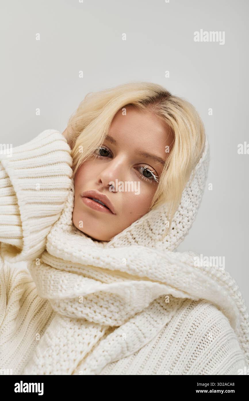 Eine schöne junge blonde Frau mit weißen Wimpern posiert in einem gemütlichen Strickpullover in einem Studio. Stockfoto