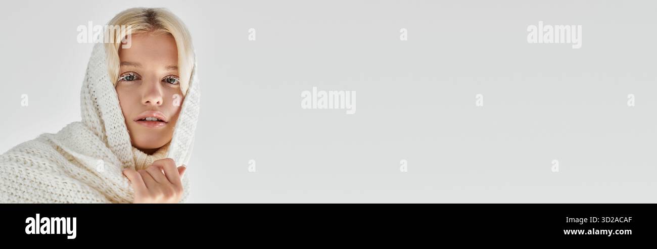 Die junge blonde Frau posiert anmutig in einem kuscheligen Strickschal, mit winterlichem Charme und Banner Stockfoto
