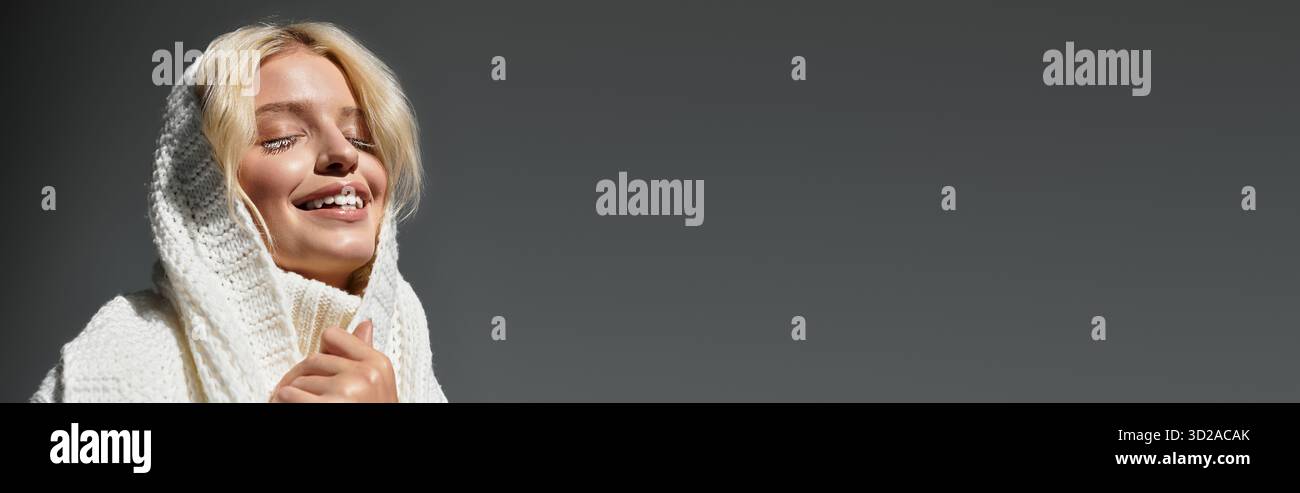 Eine junge Frau in einem weißen Pullover lächelt sanft in einem gemütlichen Studio, Banner Stockfoto