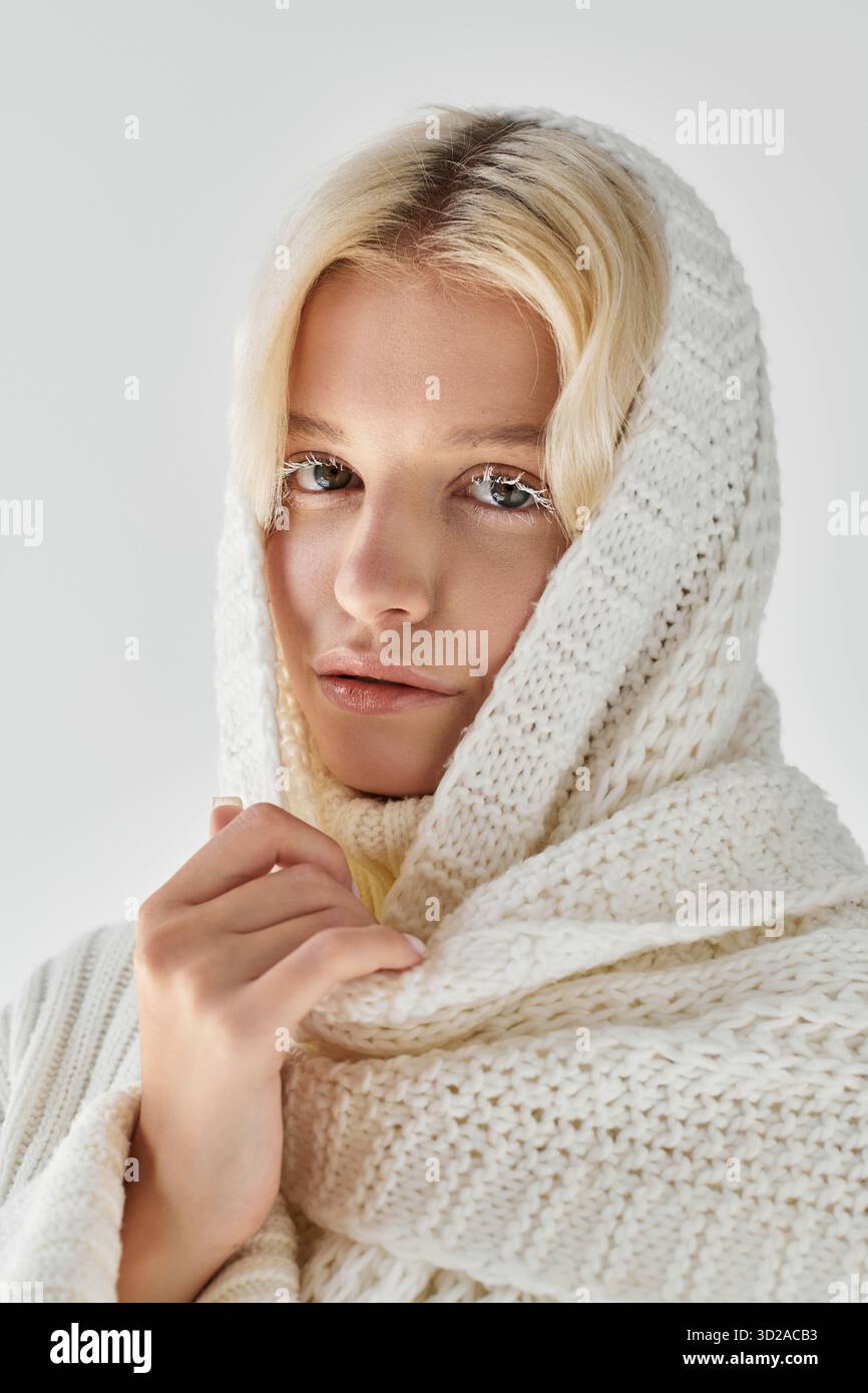 Eine junge Frau mit blonden Haaren und weißen Wimpern fängt in einem Strickschal eine gemütliche Winterstimmung ein. Stockfoto