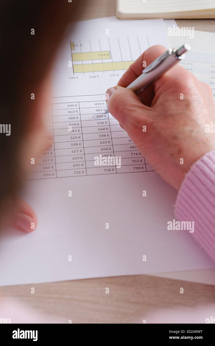 Über-Schulter-Ansicht einer Frau, die Dokumente und Finanzdaten überprüft. Der Schwerpunkt liegt auf den Dokumenten Stockfoto