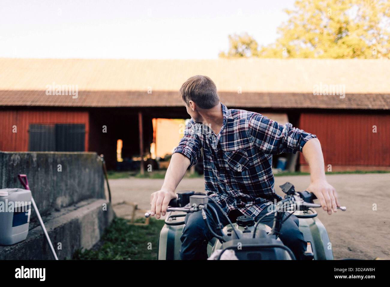 Männlicher Bauer, der über die Schulter schaut, während er auf dem Quadbike in der Scheune sitzt Stockfoto