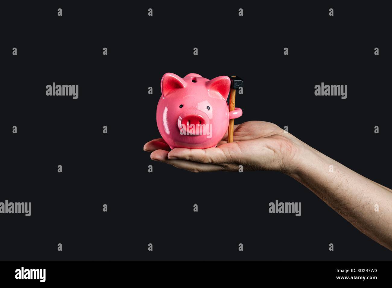 Die Hand eines kaukasischen Mannes hält eine rosafarbene Schweinebank mit einem kleinen Hammer im Schlitz, was symbolisiert, dass die Bank für einen finanziellen Notfall gebrochen wird. Stockfoto
