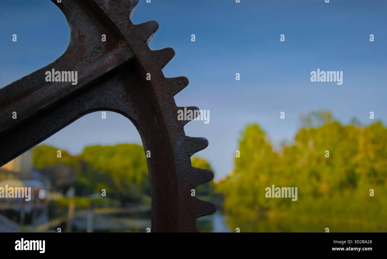 Rostige Metallausrüstung, die eine verschwommene Flusslandschaft umrahmt, industrielles Relikt mit Bokeh-Natur-Hintergrund, inspirierend für kreatives Design und Kontrast zwischen Industrie und Natur Stockfoto