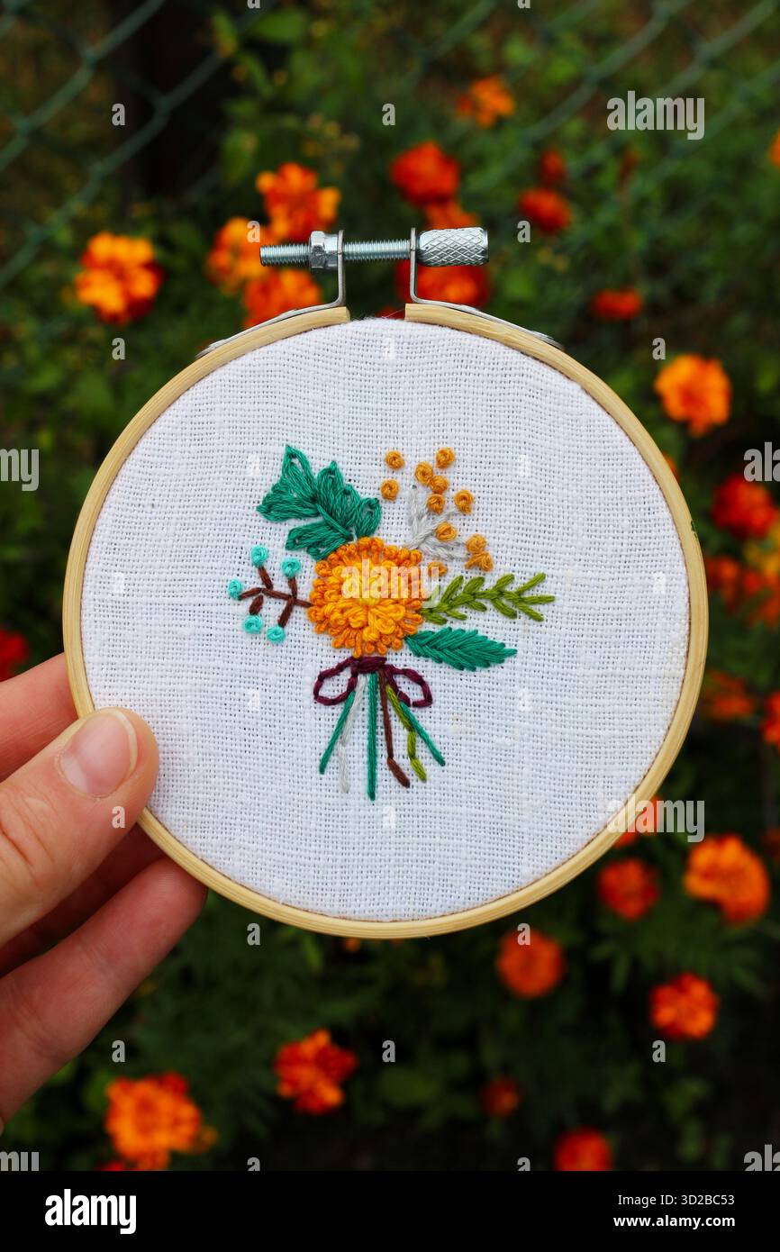 Nahaufnahme einer handgefertigten Blumenstickerei in einem hölzernen Ring mit gelbem und grünem Blumenmuster auf weißem Stoff. Stockfoto