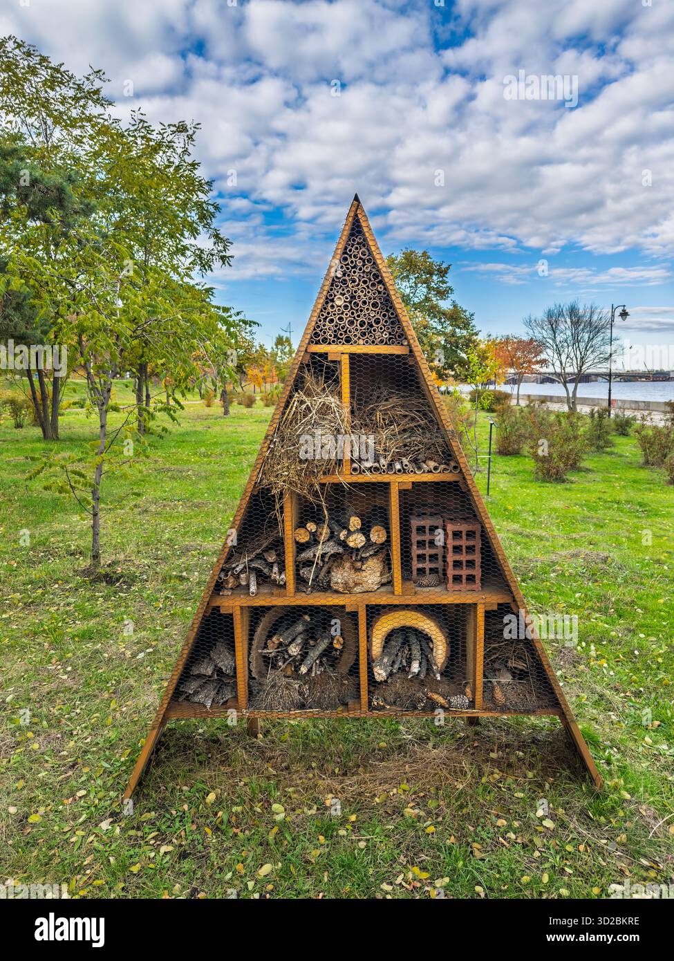 Große dreieckige Insekt-Hotelstruktur im Stadtpark in der Nähe des Sees mit natürlichen Materialien für die Biodiversität Stockfoto