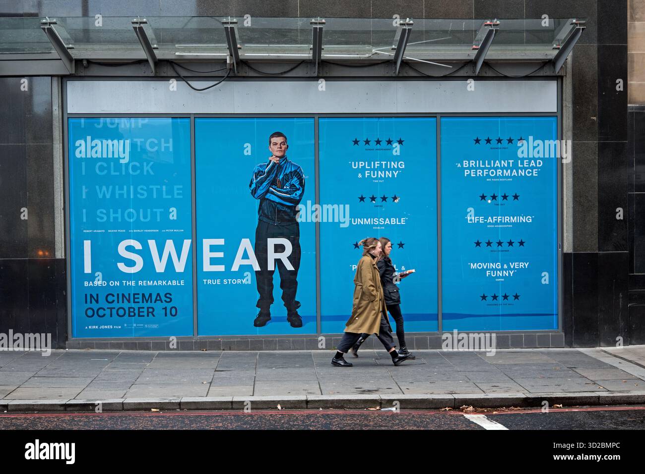 Zwei junge Frauen, die an der Werbung für den Film „Ich schwöre“ in Edinburgh, Schottland, Großbritannien, vorbeilaufen. Stockfoto