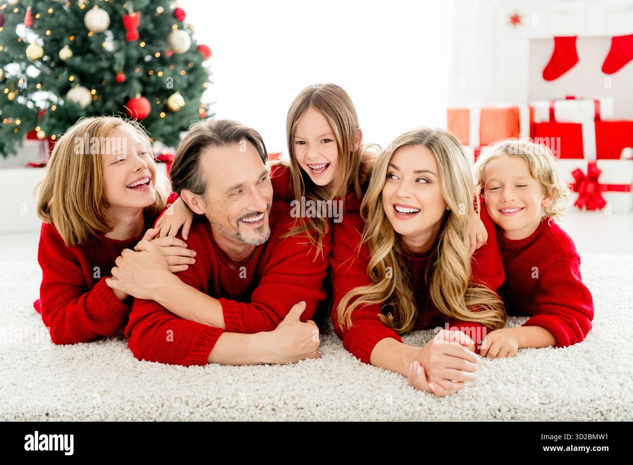 Fröhliche weihnachtszeit mit Eltern und Kindern auf einem gemütlichen Teppich neben einem beleuchteten weihnachtsbaum zu Hause Stockfoto